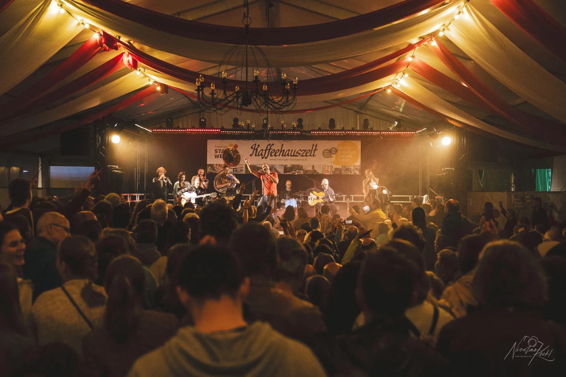 Volles Festivalzelt mit warmer Bühnenbeleuchtung und Publikum