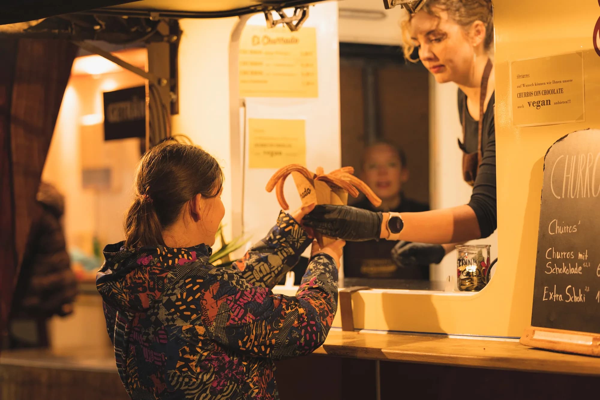 A vendor hands a customer a chocolate-covered churro at a yellow food stall.