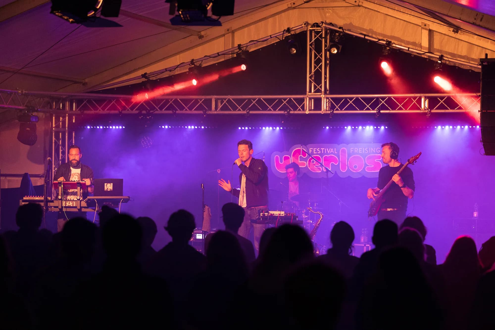 A band performs on a stage bathed in purple light with a visible Uferlos logo behind them.