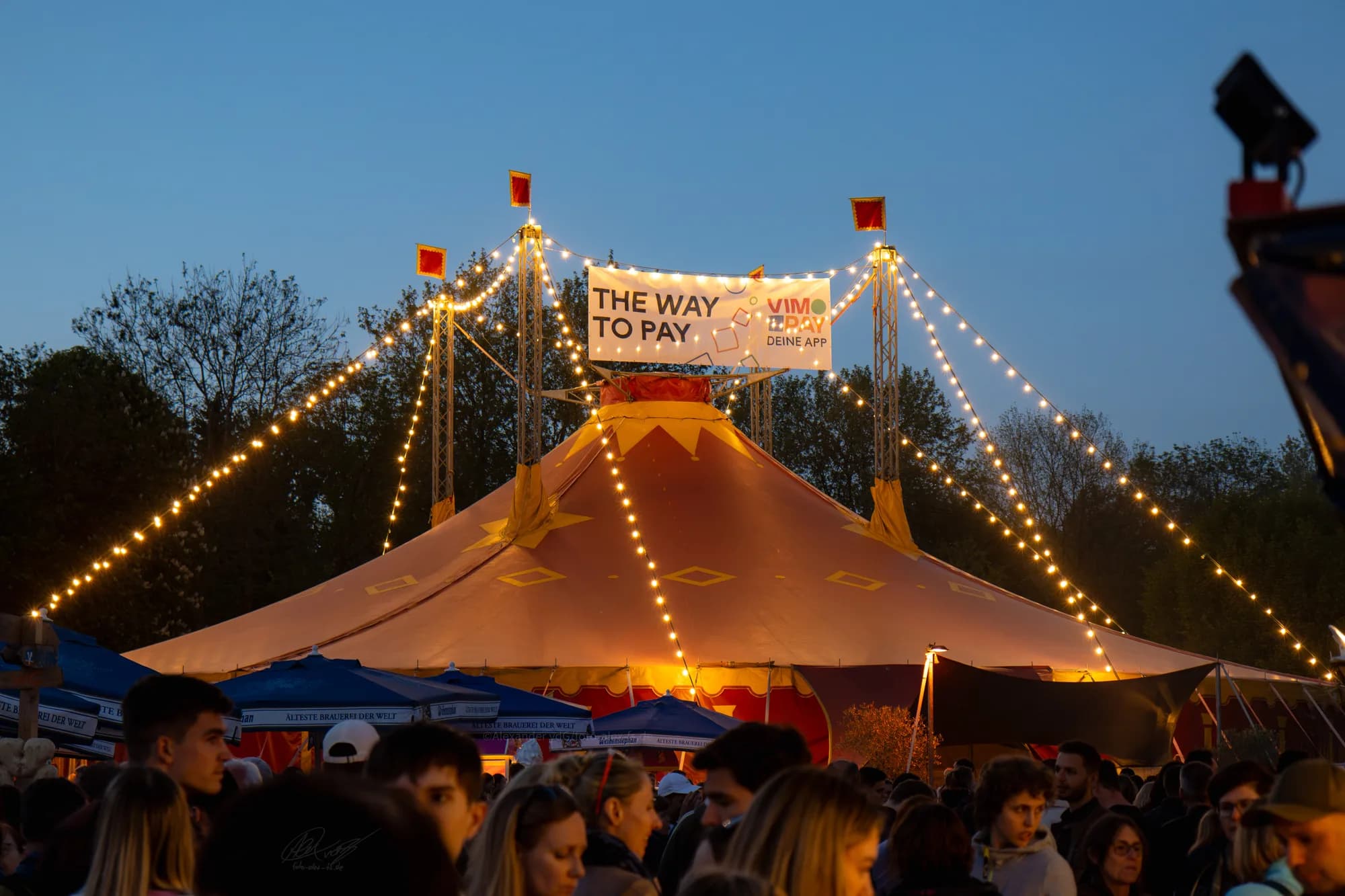 A large circus tent glowing with warm light against the evening sky at the festival grounds.