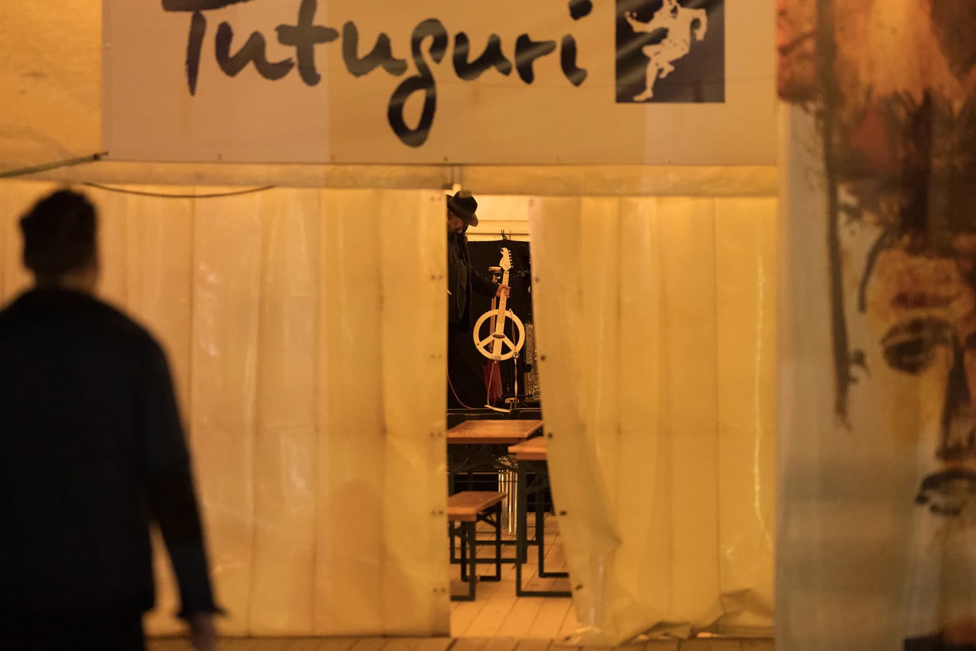A view into the Tutuguri band tent showing a guitar on a stand and a peace sign decoration through plastic curtains.